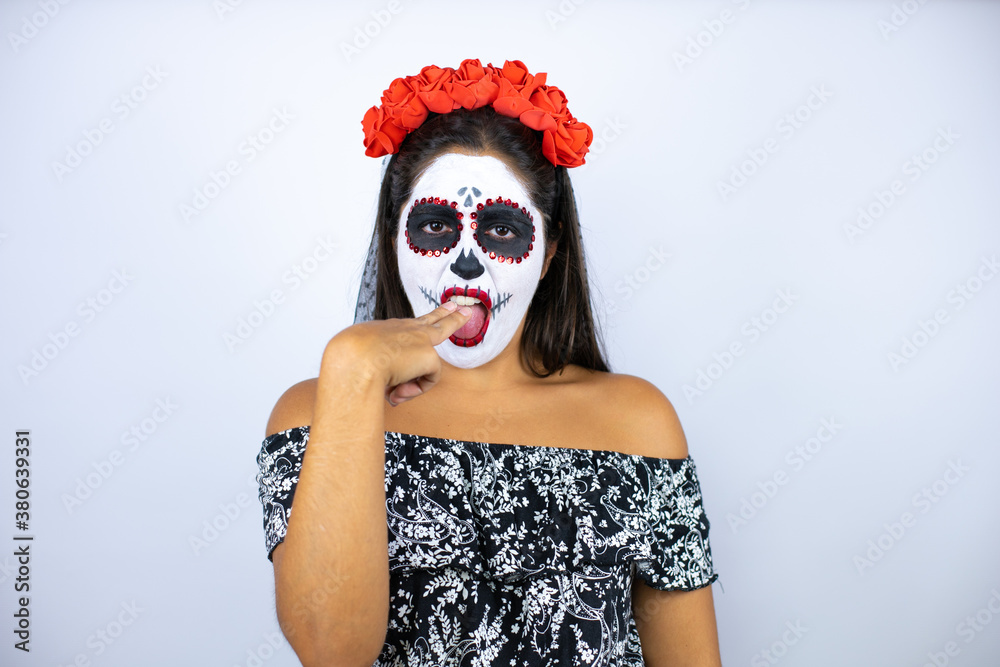 Woman wearing day of the dead costume over isolated white background disgusted with her hand inside her mouth Woman wearing day of the dead costume over isolated white background disgusted with her hand inside her mouth