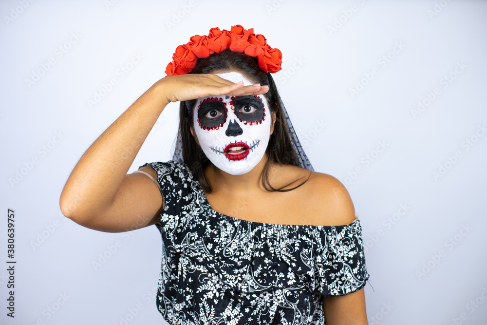 Woman wearing day of the dead costume over isolated white background very happy and smiling looking far away with hand over head. searching concept.