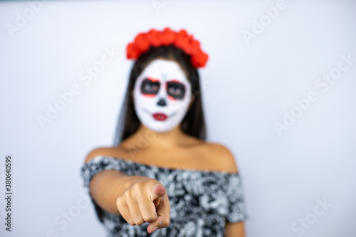 Woman wearing day of the dead costume over isolated white background pointing with finger to the camera and to you, confident gesture looking serious