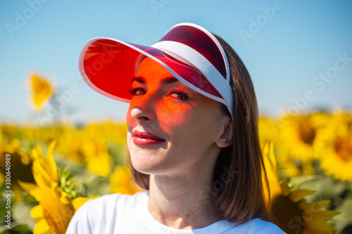 Young woman in red sun visor and white t-shirt on sunflower field photo