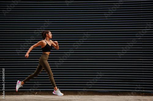 runner on the street. girl athlete with sportswear running in front of a black wall