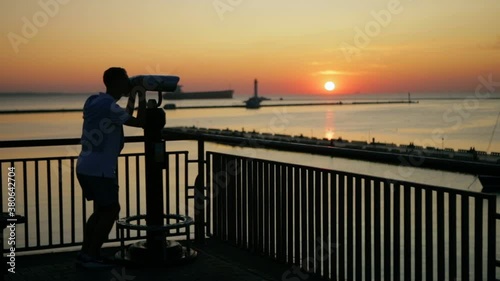 guy silhouette looks through binoculars at pictorial sun setting in orange sky reflected in endless sea water slow motion