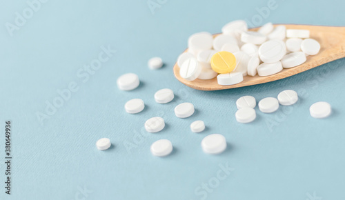 White tablets and one yellow on a wooden spoon on blue background.