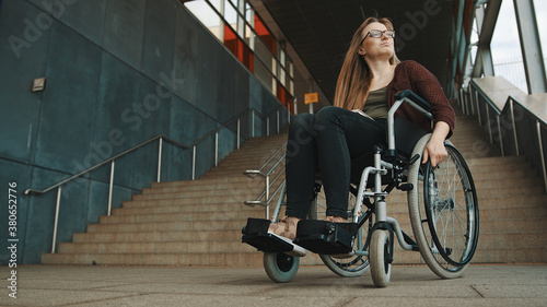 Young discouraged caucasian woman in the wheelchair in front of the staircase looking around for accessible way. High quality photo photo