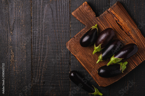 Fresh ripe eggplant on brown wooden cutting board, dark wood backdrop background, top view copy space