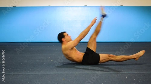 a static shot of a guy in a gymnastics gym doing ab workout with leg raises shirtless
from a side/front view photo