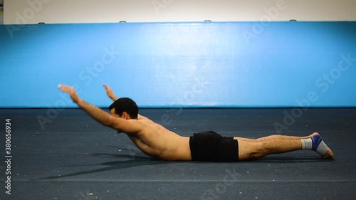 a guy doing an abs workout in a gymnastics gym
doing lying down shortless leg and hand raises
still shot photo