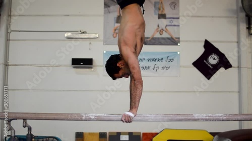 a still shot of a guy doing a handstand on the parallel bars inside a gymnastics gym photo