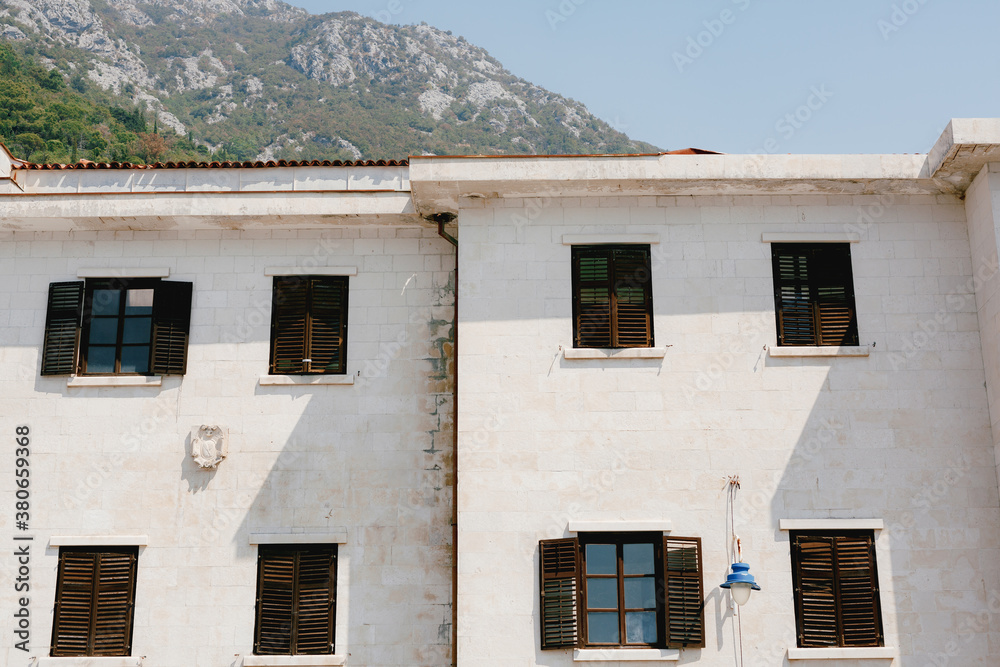 The house is white with brown windows and shutters against the backdrop of a mountainous area.