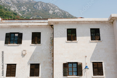 The house is white with brown windows and shutters against the backdrop of a mountainous area.