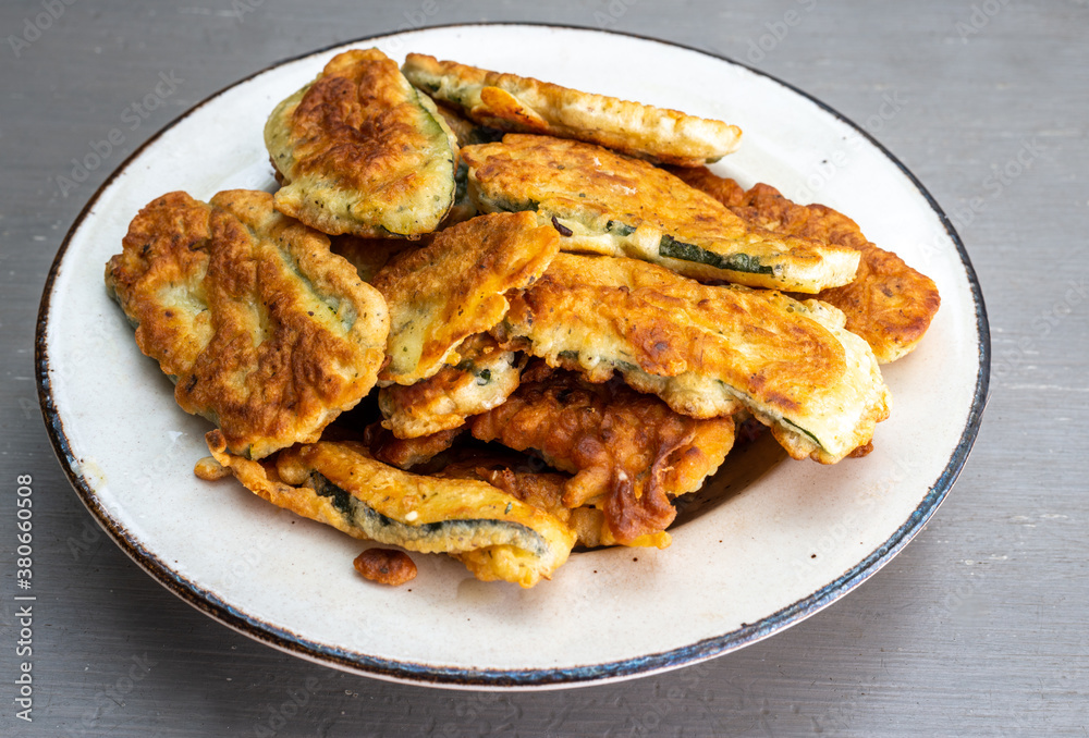 A pile of Courgette fritters in batter in a plate on grey table , A pile of Courgette fritters in batter in a plate on grey table ,