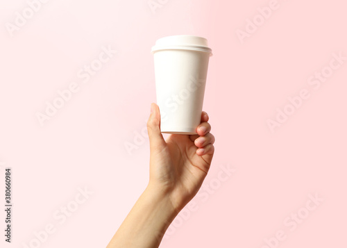 Woman holding takeaway paper coffee cup on pink background, closeup