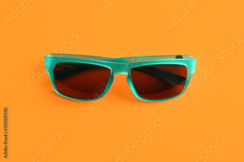 Stylish sunglasses on orange background, top view