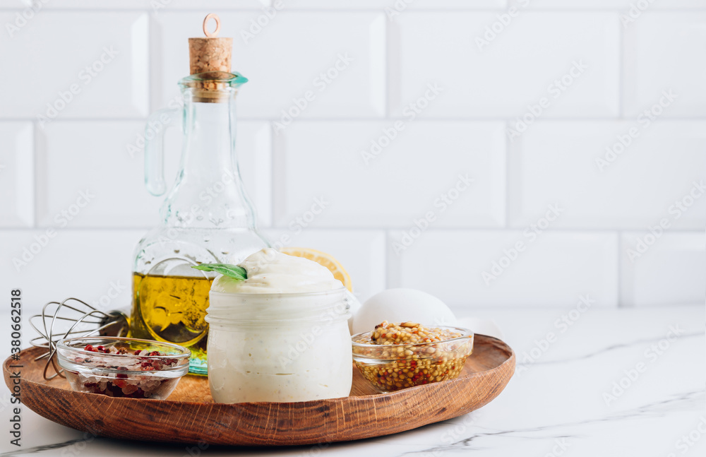 Obraz premium Homemade mayonnaise sauce with ingredient - olive oil, eggs, mustard and lemon on a wooden plate.