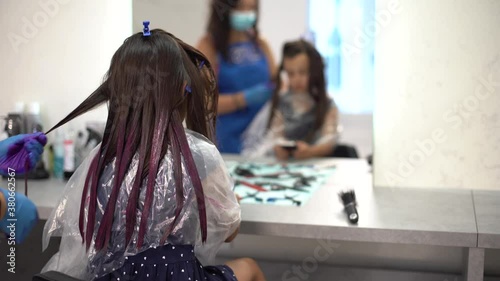 Beautiful little girl looking rubbing her chin choosing air color dye at the beauty salon photo