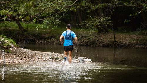 Young man in sports equipment running in mountain river