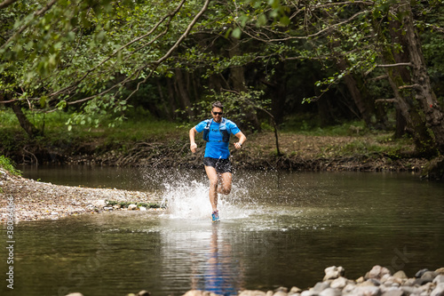 Fototapeta Naklejka Na Ścianę i Meble -  Young man in sports equipment running in mountain river