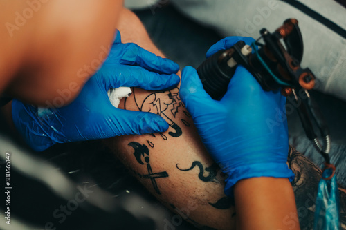 Young tattoo artist tattooing a client's leg.