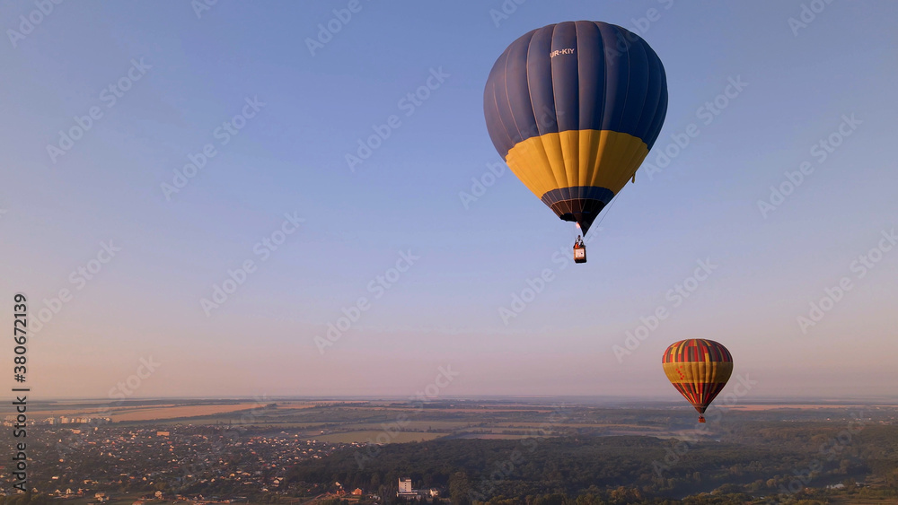 Aerial drone view of colorful hot air balloon flying over green park in small european city at summer sunrise