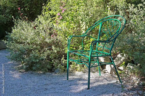 Vintage green wrought iron armchair in an alcove of a path among tropical garden flowers in sunshine