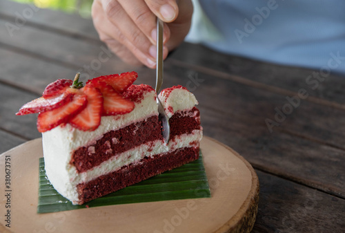 People are scooping red velvet cakes and fresh strawberries on round wooden trays to eat.
