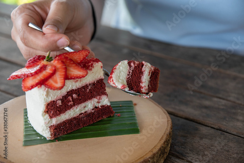People are scooping red velvet cakes and fresh strawberries on round wooden trays to eat.
