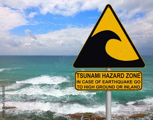 Tsunami warning and evacuation sign located on a beach. The sea and blue sky as background