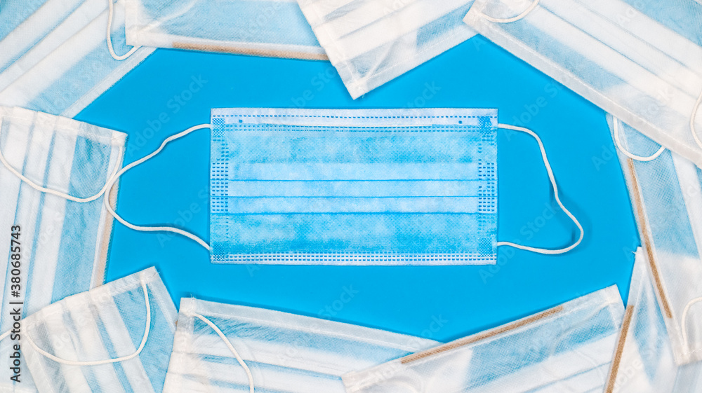 Coronavirus protection. Many antiviral protective medical face masks with ear loops spread out on a blue background. Surgical mask background. Respiratory syndrome, coronavirus disease COVID-19. Coronavirus protection. Many antiviral protective medical face masks with ear loops spread out on a blue background. Surgical mask background. Respiratory syndrome, coronavirus disease COVID-19.