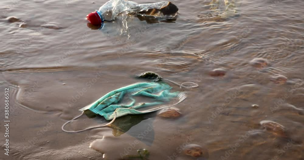medical face mask in the sea coast, plastic waste pollution since coronavirus covid-19 pandemic