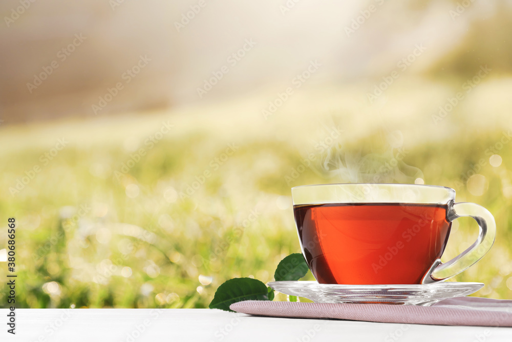 Glass cup of fresh hot tea on wooden table against blurred field. Space for text Glass cup of fresh hot tea on wooden table against blurred field. Space for text