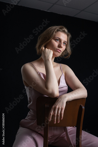 portrait of young pensive caucasian woman with short hair posing in pink suit, sitting on chair in front of black background. model tests of pretty lady in blouse, trousers. attractive female poses © Artem Zatsepilin