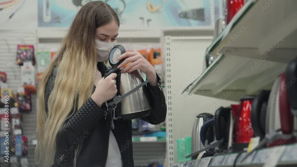Young lady in medical mask buying an electric kettle in hypermarket Young lady in medical mask buying an electric kettle in hypermarket