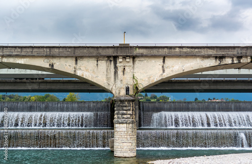 Obraz na plátně View from below of the ancient bridge and the cascade of water that crosses the dam barrier