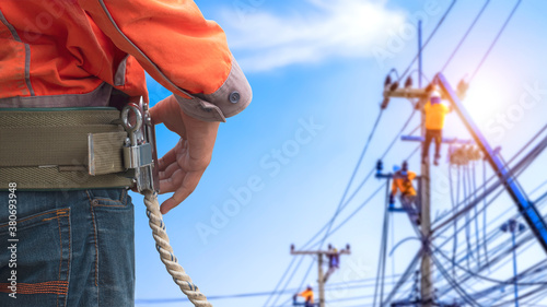 Midsection of electrician lineman wearing safety belt with blurred background of electrical workers team are working on power poles in public area photo