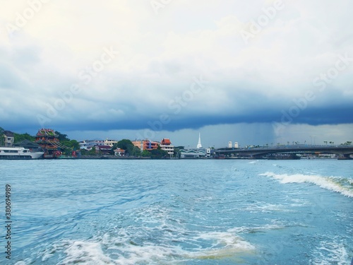 Bangkok, the capital of Thailand, large city. Panoramic view from Chao Phraya River. View of buddhist temples, buildings and bridge in a distance. Blue water, sky with clouds before rain, thundercloud © Oxana