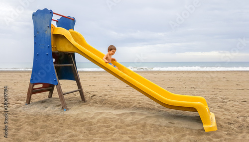 Baby boy sliding down a yellow slide on the beach