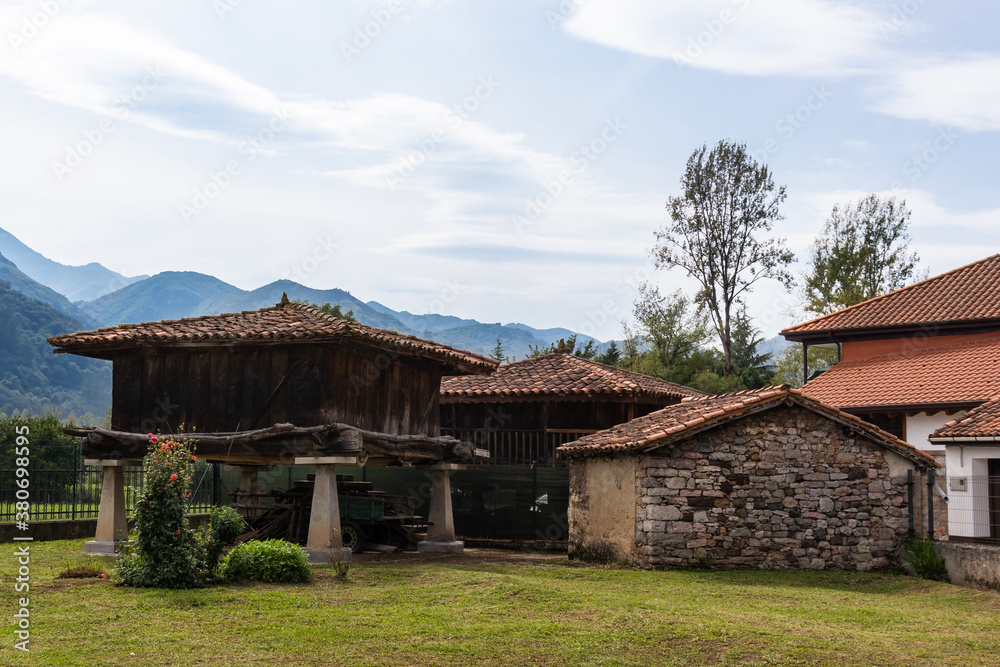 Hórreo, traditional granary from the North of Spain, built in wood and stone on four pillars that raise the horreo from the floor. Surrounded by traditional stone houses. Asturias, North Spain Hórreo, traditional granary from the North of Spain, built in wood and stone on four pillars that raise the horreo from the floor. Surrounded by traditional stone houses. Asturias, North Spain