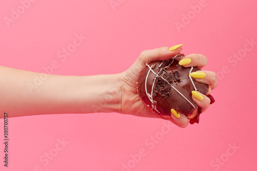 Woman with yellow nails squeezes a chocolate doughnut in her hand photo