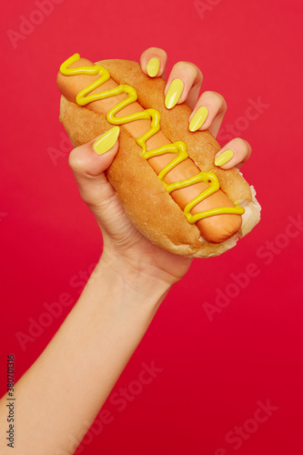 Woman's hand with yellow painted nails holds hotdog photo