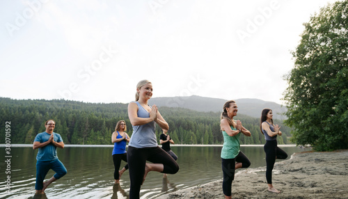 A group class of people practicing yoga outside at the lake in s
