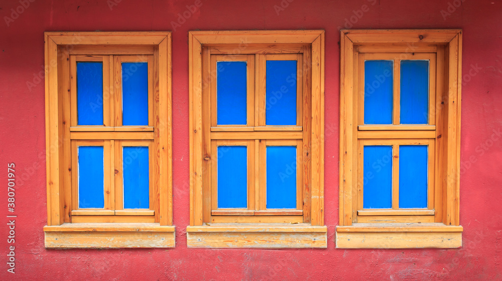 Three wooden windows on old red wall. Blue colors on windows. Historical house wall.