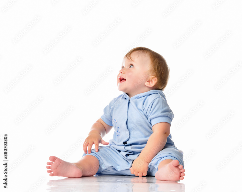 Baby in blue jumpsuit sitting on floor looking up Baby in blue jumpsuit sitting on floor looking up