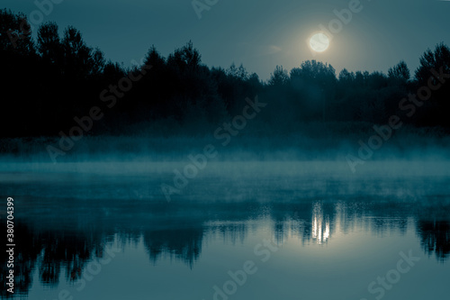 Night mystical scenery. Full moon over the foggy river and its reflection in the still water. © stone36