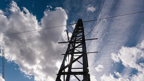 Time-lapse of the industrial green energy electric grid tower transmitter silhouette with blue clouds over it. Timelapse sunset background with high voltage power line.