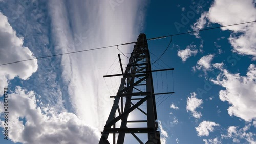 Time-lapse of the industrial green energy electric grid tower transmitter silhouette with blue clouds over it. Timelapse sunset background with high voltage power line.
