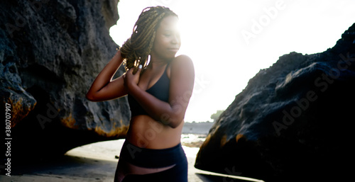 Young ethnic woman in sportswear with eyes closed standing on rocky coast