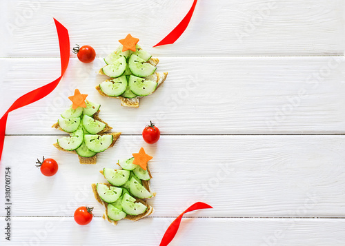 A creative idea for decorating New Year's snacks. Sandwiches in the form of a Christmas tree with a cucumber and a carrot star, cherry tomatoes on a white background. Vegetarian and dietary concept
