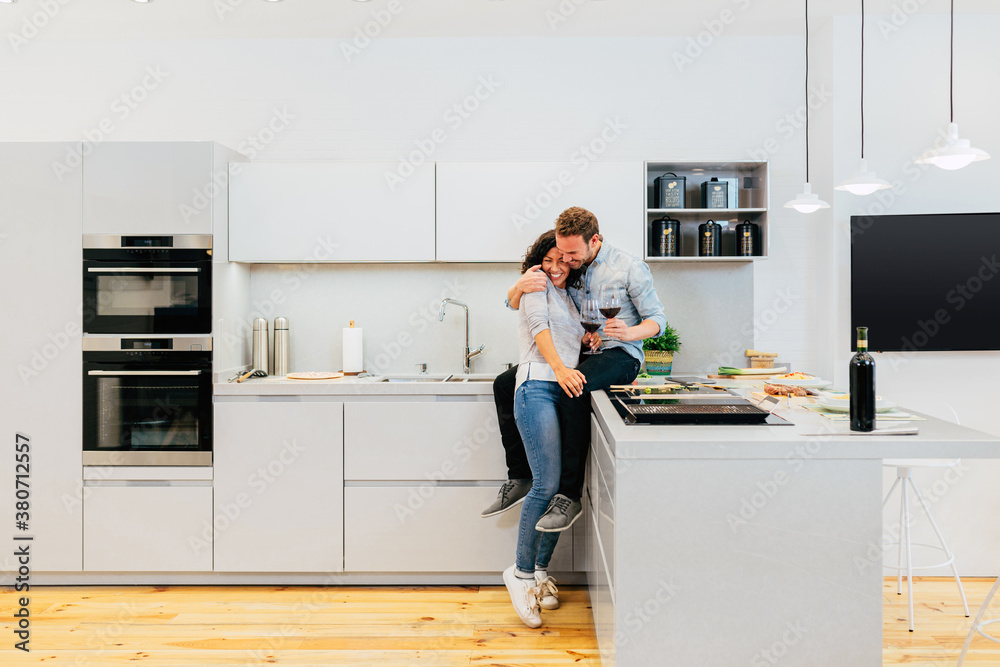 Happy couple with wine hugging in modern kitchen Happy couple with wine hugging in modern kitchen