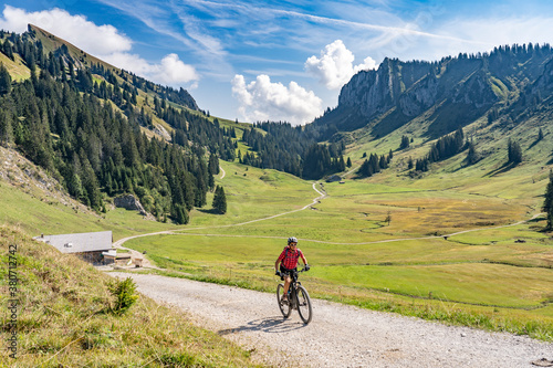 nice senior woman riding her electric mountain bike up to the Schreiber Sattel below Winterstaude summit in the Bregenzer Wald mountain range in Vorarlberg, Austria