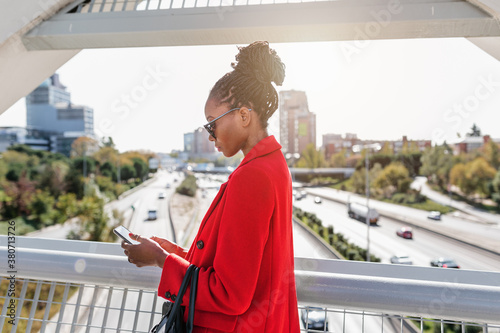 Pensive elegantly dressed black woman browsing smartphone in street